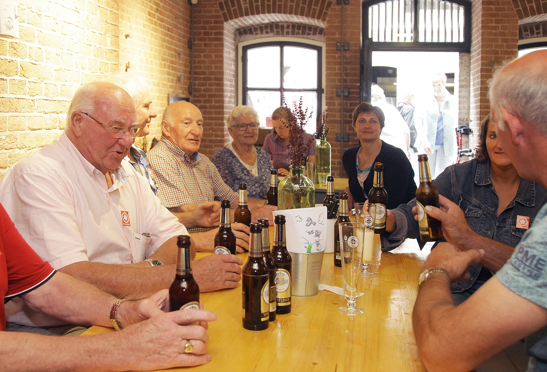 Vrijwilligers van Fort Pannerden zitten met een hoop mensen om een tafel, op de tafel staan wat lekkere drankjes.