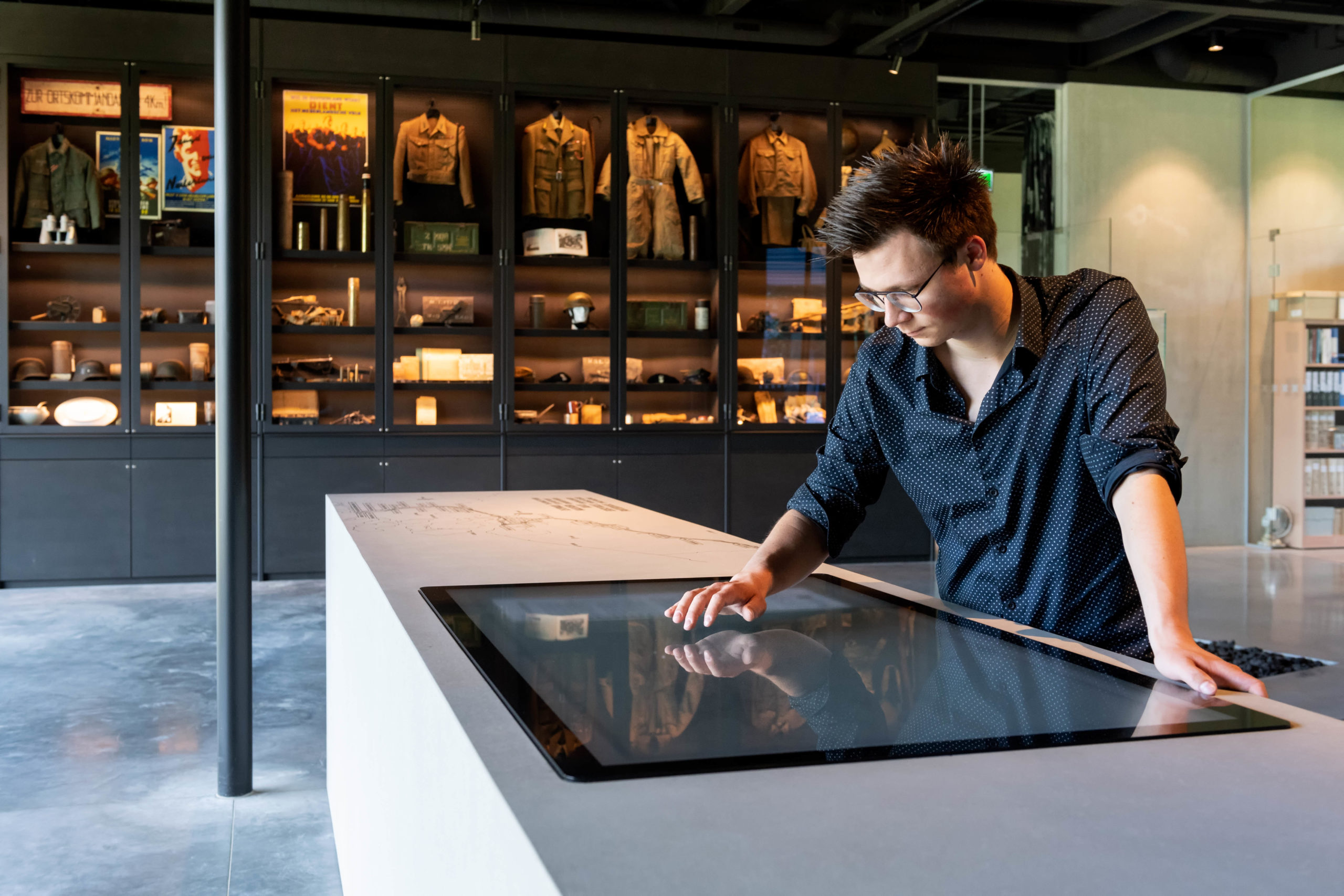 Een bezoeker in een museum kijkt neer op een groot scherm dat in een soort witte tafel bevestigd is.