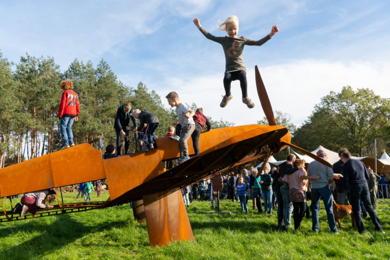 Kinderen spelen buiten op een replica van een gevechtsvliegtuig gemaakt van cortenstaal.
