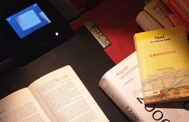Drie boeken op een bureau over het Gronings, waarvan een boek opengeslagen op een scanapparaat.