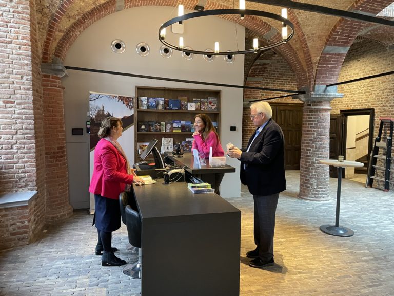 Twee vrijwilligers ontvangen een bezoeker aan de balie van Museum Kasteel Wijchen
