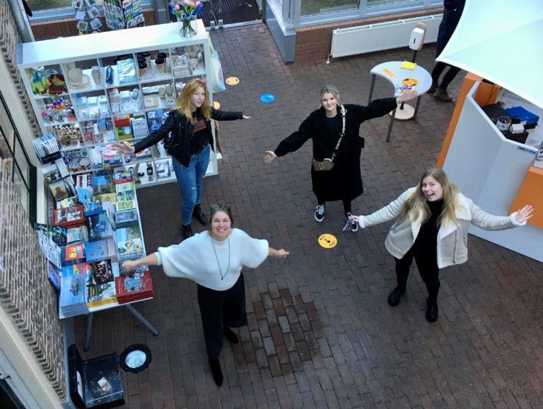 Het educatieteam van vier jonge vrouwen staat in de museumwinkel met hun armen gespreid om nieuwe vrijwilligers te verwelkomen.