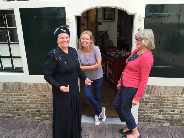 Drie vrijwilligers van Streekmuseum Goeree-Overflakkee poseren buiten het museum en hebben veel lol met elkaar.